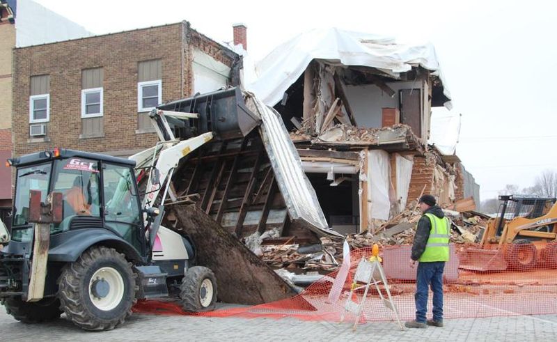 GCI loader tearing down a two-story brick building behind safety fencing